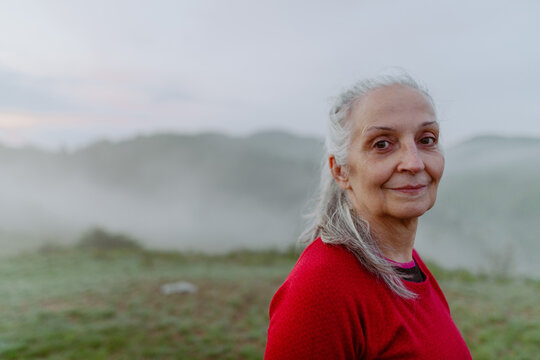 Senior woman hiking in nature on early morning with fog and mountains in background.