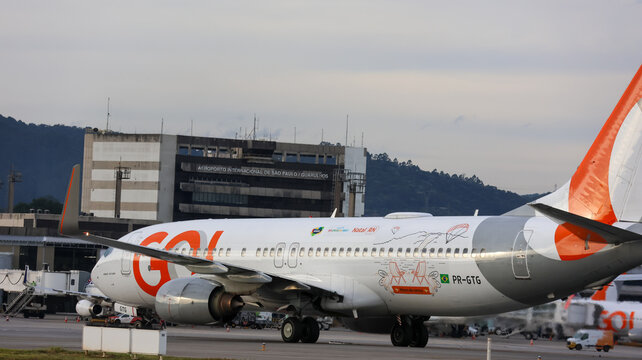 Avi&atilde;o da GOL parado em &aacute;rea operacional do aeroporto, com fuselagem lateral e estrutura do terminal ao fundo. Guarulhos SP em 09 Maio 26