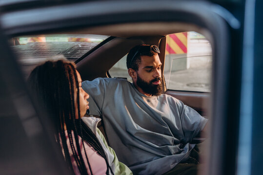Happy young African American couple listens to hip hop music and sits in car on parking site
