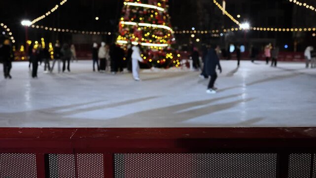 People ice skating at night under festive lights near a Christmas tree