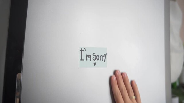 Video of a woman&rsquo;s hands placing an &ldquo;I&rsquo;m Sorry&rdquo; note on a home refrigerator. Apology and emotional communication concept.

