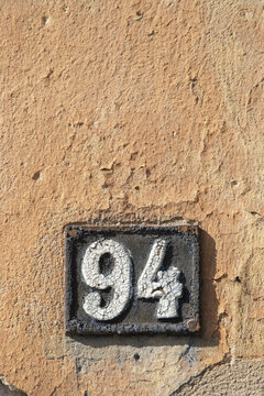 Weathered cast iron house number 94 on cracked orange wall with vertical copy space for design.