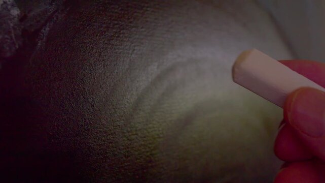  A macro shot with shallow depth of field showing a hand using white chalk to write a formula or logical equation on a blackboard, representing education, science, and problem-solving.
