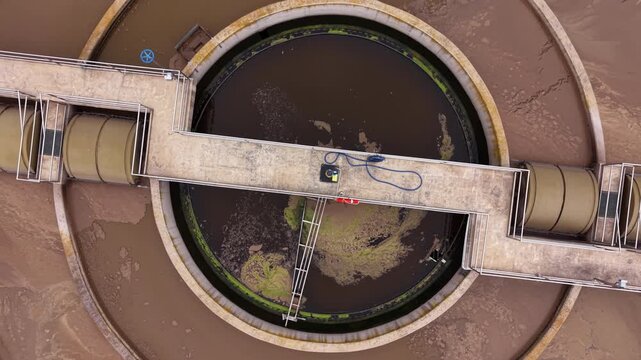Top-down view of a circular secondary clarifier surrounded by an aeration basin at a municipal wastewater treatment facility, showing concentric treatment rings and access bridge