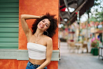 Fototapeta premium A portrait of young happy latina woman posing by a colorful wall in the street outdoors