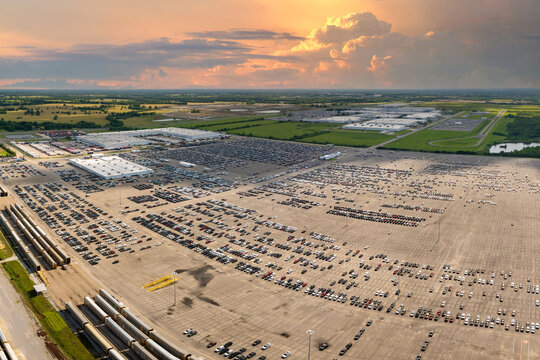 Industrial cargo trains at automotive factory loaded with new cars ready for transporting. Automaker parking lot with vehicles for sale