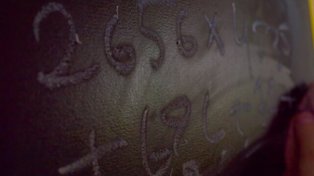 Close up of hand erasing numbers from chalkboard with wet rag.A macro shot with shallow depth of field showing a hand wiping away chalk numbers from a blackboard using a damp cloth, leaving wet streak
