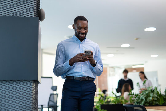 Black businessman smiling holding smartphone in modern office