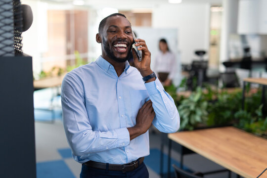 Black businessman communicating on phone, smiling in office