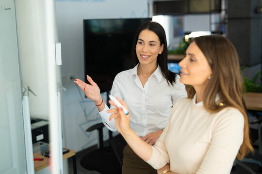Businesswomen collaborating on whiteboard presentation in modern office