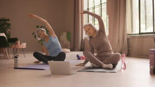 Slim senior women practicing yoga while following online fitness tutorial