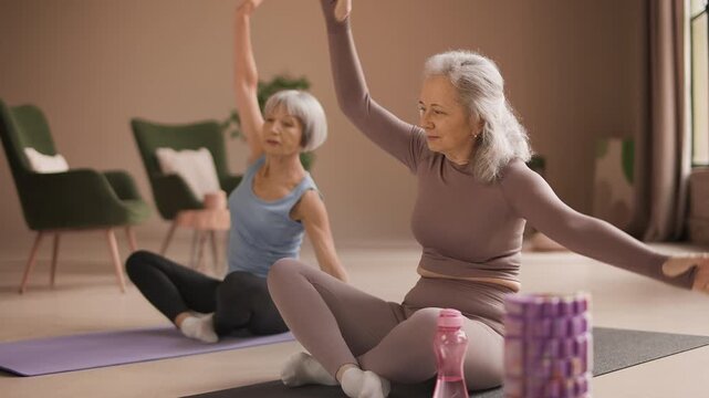 Senior female friends watching fitness tutorial while doing stretching exercises