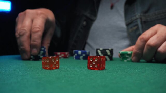 Player rolls dice and places poker chips on green felt table during a game night with colorful chips and dice in a dimly lit setting