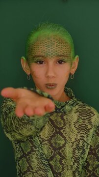 A teenage girl with a painted face in the guise of a green snake. Halloween Outfit