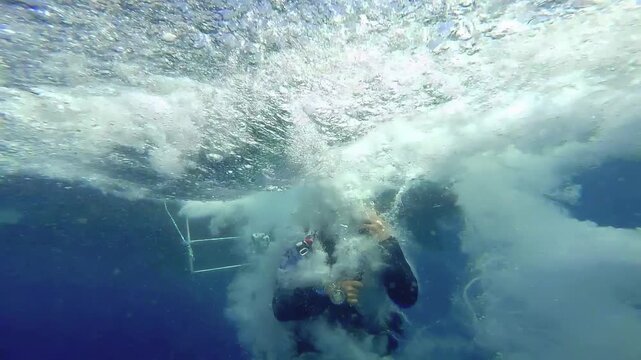 Scuba Diver Jumping Off Boat into Ocean Underwater Split Shot Slow Motion. The shot captures the massive splash, turbulent white water, and a cloud of air bubbles surrounding the diver underwater.