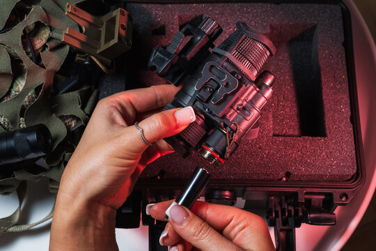 Close-up of a woman inserting a battery into a professional image intensifier tube night vision monocular with a tactical hard case