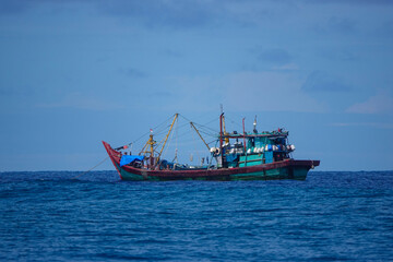 Obraz premium Traditional wooden fishing boat floating on calm tropical water near the Mentawai Islands. Working vessel sits alone against a soft blue horizon. Everyday marine life in remote parts of Indonesia.