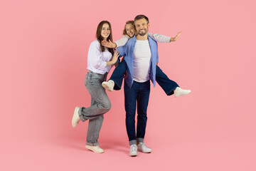 Obraz premium Cheerful caucasian family having fun together on pink studio background, posing playfully in a modern parenting and happy lifestyle concept portrait