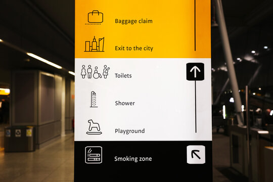 Airport information sign with baggage claim and public facilities symbols. Modern terminal direction board showing toilets shower playground and smoking zone indoors at night terminal