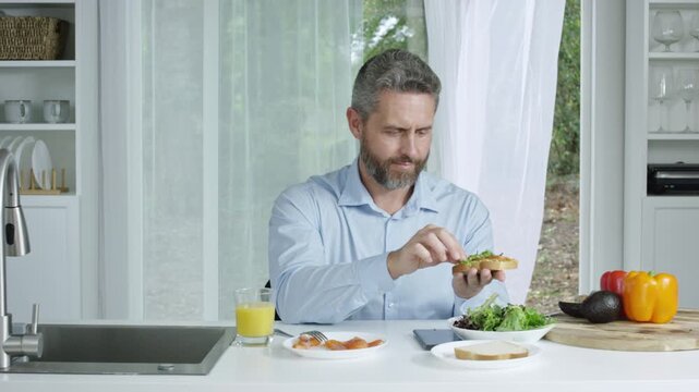 Man making a balanced breakfast in the kitchen. Kitchen morning routine showing a man and healthy lifestyle. Man preparing a fresh salad in the kitchen in the morning.