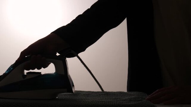 Man's silhouette using an iron to press clothes, performing domestic chores and daily routine tasks, highlighting the concept of household work and daily life