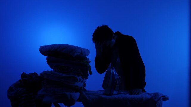 Stressed man silhouette ironing a towering pile of laundry on a blue background, conveying exhaustion, overwhelm and the burden of unpaid domestic work and household routine