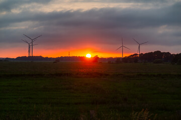 Obraz premium Dramatic sunrise over wind turbines in rural green landscape under dark storm clouds, conceptualizing sustainable energy and climate change transition 