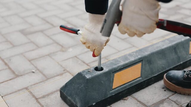 Worker fastening rubber parking wheel stop on tiled pavement close up