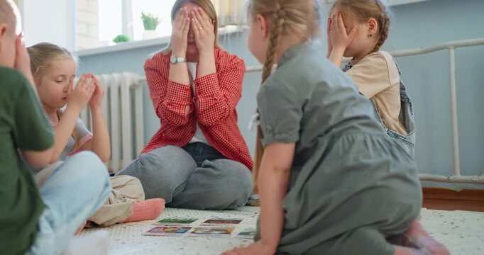 Teacher guiding young children in a classroom floor activity, using picture cards for collaborative learning, discussion, and playful early education