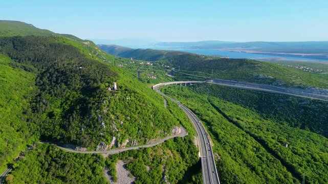 Aerial view of Croatia's lush green hills, winding highway A7, and the stunning Kvarner Gulf with islands under a clear spring sky.