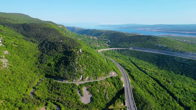 Aerial view of Croatia's lush green hills, winding highway A7, and the stunning Kvarner Gulf with islands under a clear spring sky.