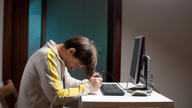 Man holding a console controller with his head down experiencing frustration and defeat while playing an intense video game in front of a computer monitor, showing signs of addiction and despair