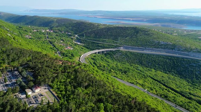 Aerial view of the modern highway A7 winding through lush green hills towards the serene Kvarner Gulf. A vibrant spring landscape perfect for a scenic drive along the Adriatic coast. Hreljin