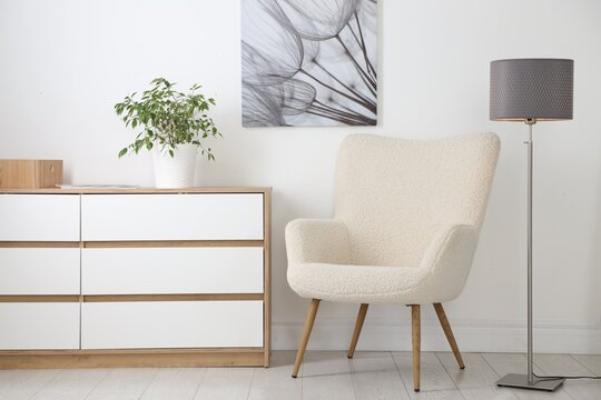 Stylish floor lamp, armchair, dresser and houseplant indoors. Interior design