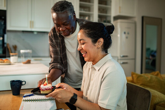 Smiling woman receives birthday cupcake from man in home kitchen