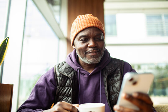 Smiling mature man texting on smartphone in cafe
