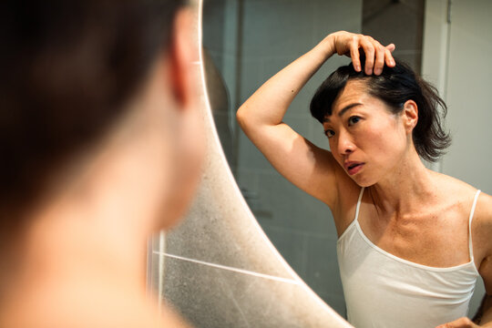 Woman examining scalp in bathroom mirror at home