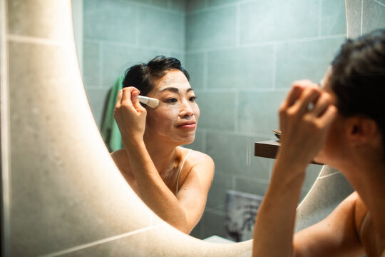 Woman applying face mask in bathroom mirror
