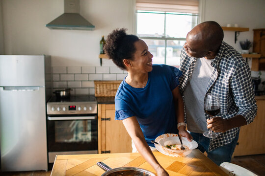 Happy couple cooking and sharing wine in a home kitchen