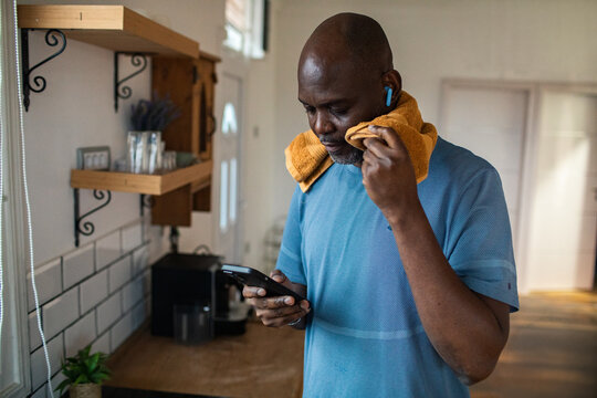 Man wiping sweat and checking smartphone after workout in home kitchen