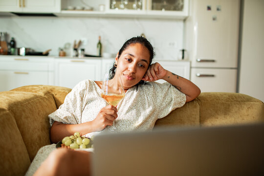 Woman relaxing on sofa with wine while watching laptop at home