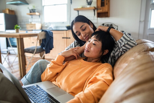 Two women relaxing with laptop on sofa at home together