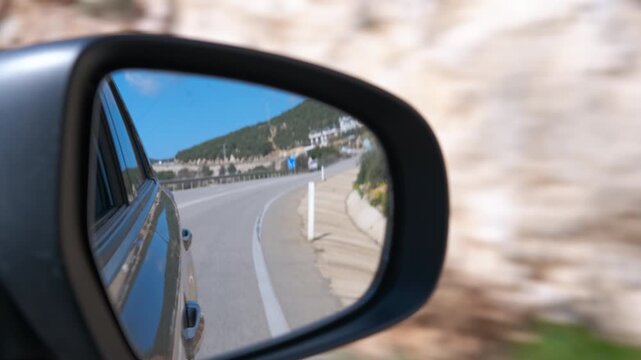 Driving car reflecting winding coastal road in side mirror. Scenic view of a beautiful coastal road and landscape reflected in a moving car's side-view mirror, capturing the essence of a road tri