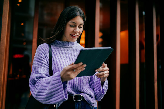 Successful woman using tablet device in modern office corridor with wooden walls. Digital nomad browsing online, creative designer working remotely, modern IT business concept, wireless connection.
