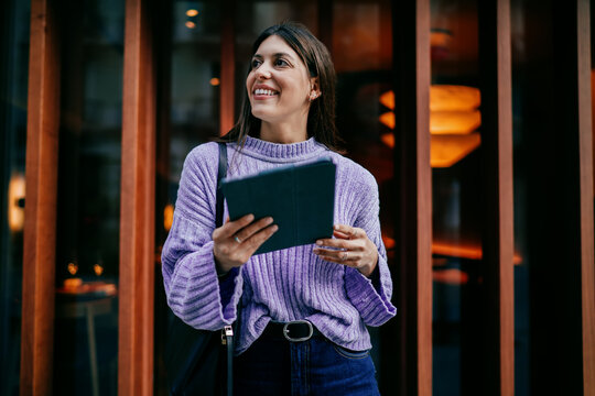 Thoughtful young woman looking away holding tablet and electronic pencil. Concept of dreaming, vision, career growth, digital planning. Female freelancer working in modern workspace environment.