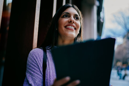 Smiling female user typing on digital tablet with stylus in hand. Financial technology, online banking, data processing or creative editing. Modern professional working in wooden textured office.