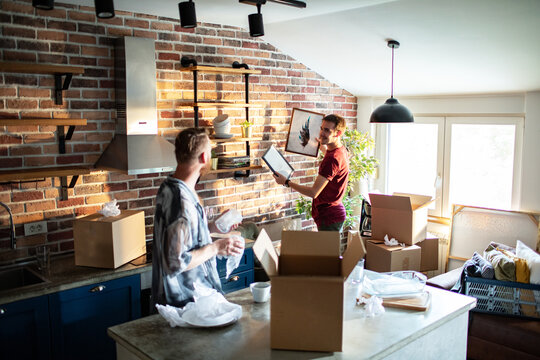 Two men unpacking boxes and hanging artwork in modern kitchen