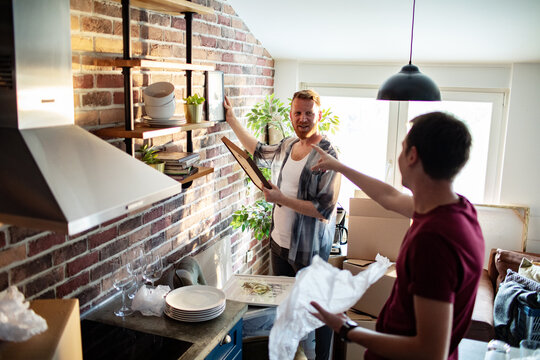 Two men unpacking and decorating shelves in modern kitchen