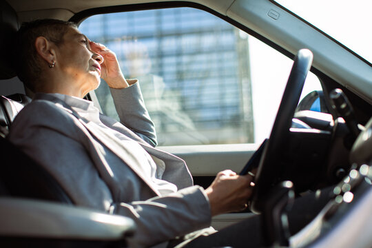 Stressed mature businesswoman rubbing forehead in car interior