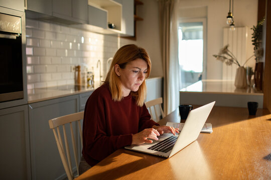 Woman working on laptop at home kitchen table